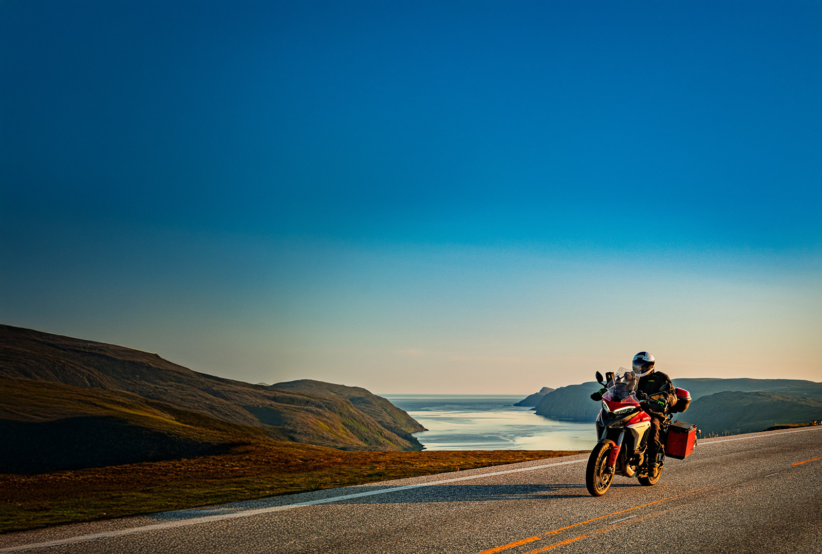 Un motociclista col sole di mezzanotte a Capo Nord su una strada panoramica affacciata sul Mare del Nord
